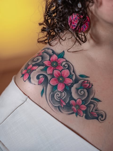 Flores rosadas con hojas verdes y formas grises tatuadas en hombro y pecho